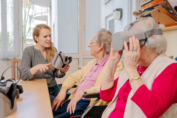 Zwei Seniorinnen mit VR-Brillen, Gründerin Roxana Hennig erklärt die Technik