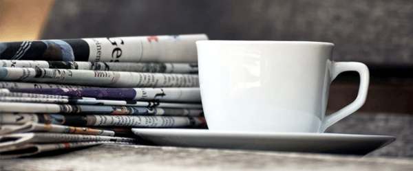 Foto zeigt einen Zeitungsstapel neben einer Kaffeetasse